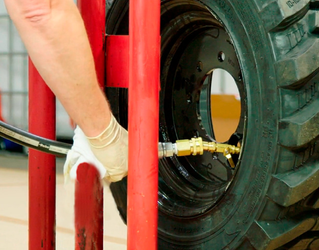 Acercamiento al proceso de llenado de una llanta industrial con polímero de poliuretano, mostrando la boquilla de inyección conectada a la válvula.