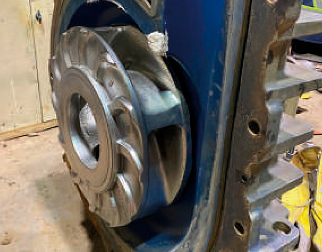 Primer plano del interior de una bomba industrial desensamblada, mostrando un impulsor metálico de color gris en el centro de una carcasa de color azul.