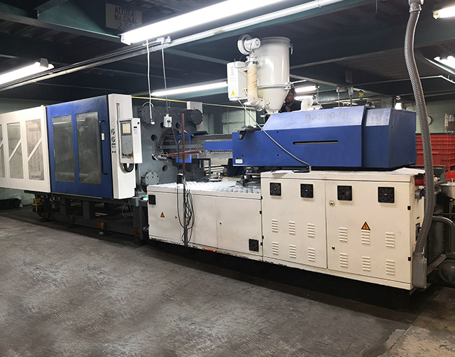 Máquina de inyección de polímeros horizontal con un silo de alimentación en la parte superior, operando en una fábrica de Taza Polymer.