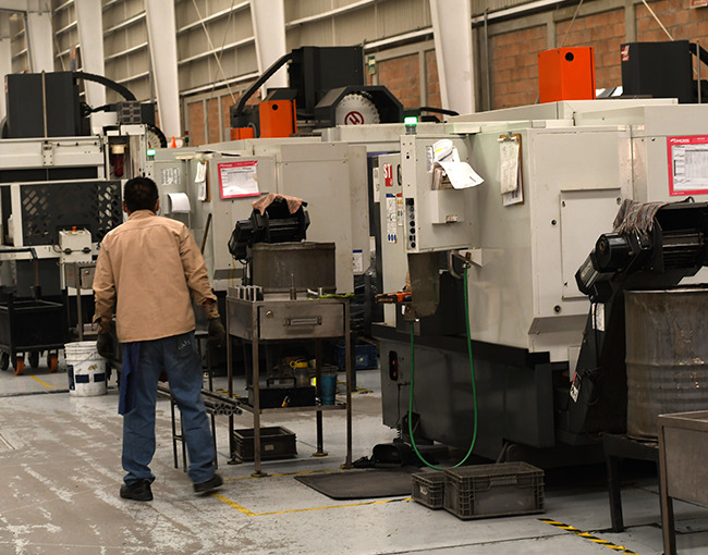 Un trabajador en una fábrica industrial camina entre varias máquinas CNC, mostrando el entorno de producción de alta tecnología de la empresa.