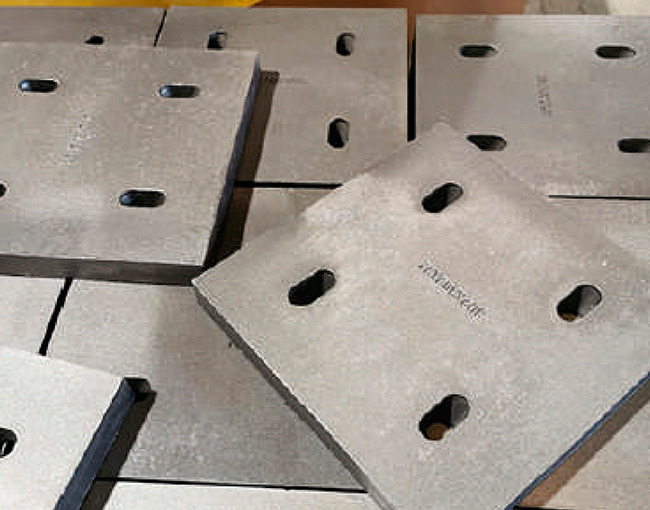 Un montón de placas de metal cuadradas y gruesas con orificios ovalados, típicas de componentes de maquinaria pesada que requieren protección contra el desgaste y el impacto.