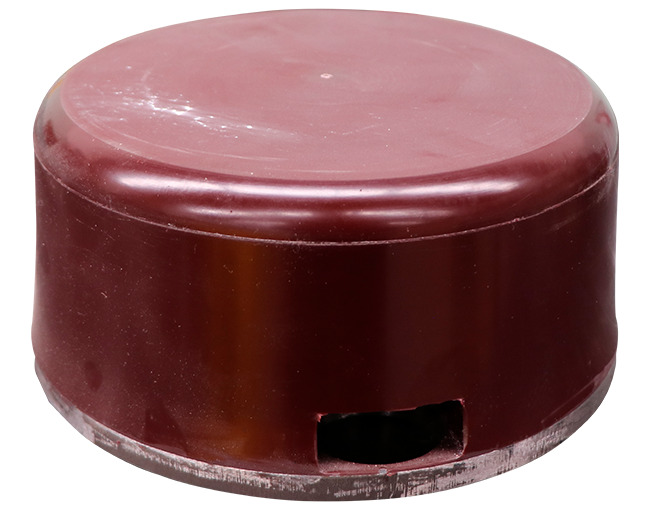 Un componente cilíndrico o disco de poliuretano de color marrón oscuro o rojo ladrillo. El objeto tiene bordes redondeados en la parte superior y una superficie ligeramente pulida o con polvo. Una abertura rectangular se encuentra cerca del borde inferior, exponiendo el interior del objeto. La parte inferior parece tener un acabado ligeramente diferente, como si hubiera sido cortado.