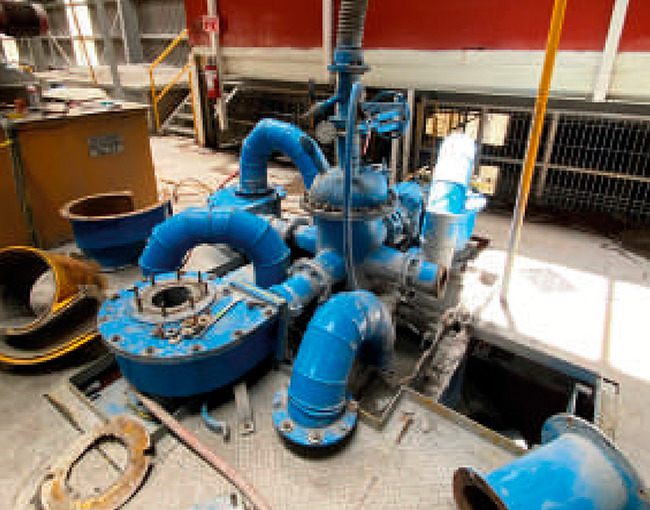 Componentes de una bomba industrial y un sistema de tuberías de color azul, parcialmente desensamblados en un taller.