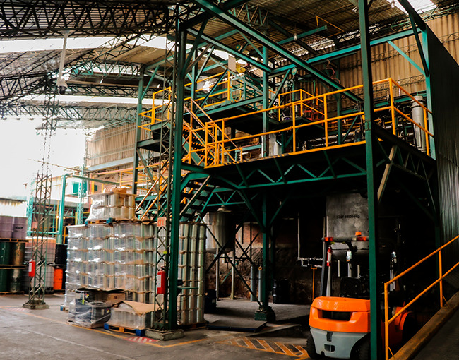 Planta industrial de procesamiento de productos químicos con grandes tanques, tuberías y una estructura de acero, mostrando las instalaciones de fabricación de Taza Polymer.