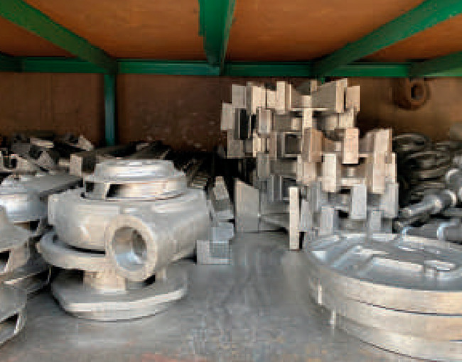 Estantes con piezas industriales de metal fundido, incluyendo impulsores de bombas y otros componentes de maquinaria pesada.