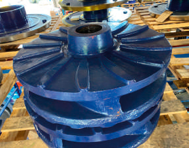 Una pila de grandes impulsores o aspas de bomba de color azul, colocados sobre un pallet de madera en un entorno de almacén industrial.