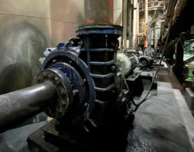 Bomba industrial de gran tamaño en un entorno de fábrica, con tuberías metálicas y un motor en el fondo.