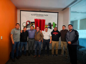 Un equipo de empleados de Taza Polymer posa sonriendo en una convención de ventas, frente a una pantalla con la marca de la empresa y el lema "PASIÓN POR INNOVAR".